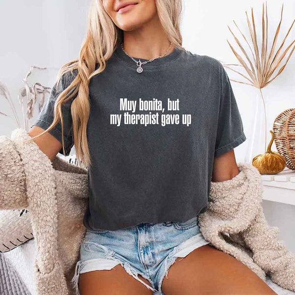 May include a person wearing a pepper colored sarcastic graphic t-shirt with the phrase “Muy Bonita But My Therapist Gave Up”.

