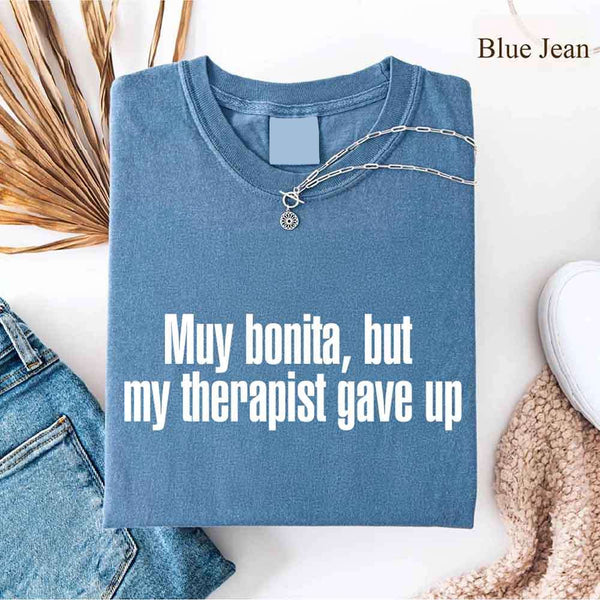May include a person wearing a blue jean colored sarcastic graphic t-shirt with the phrase “Muy Bonita But My Therapist Gave Up”.
