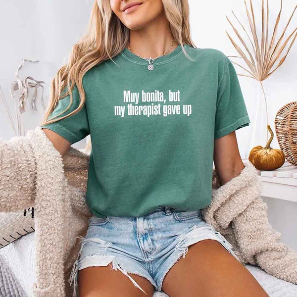 May include a person wearing a light green colored sarcastic graphic t-shirt with the phrase “Muy Bonita But My Therapist Gave Up”.
