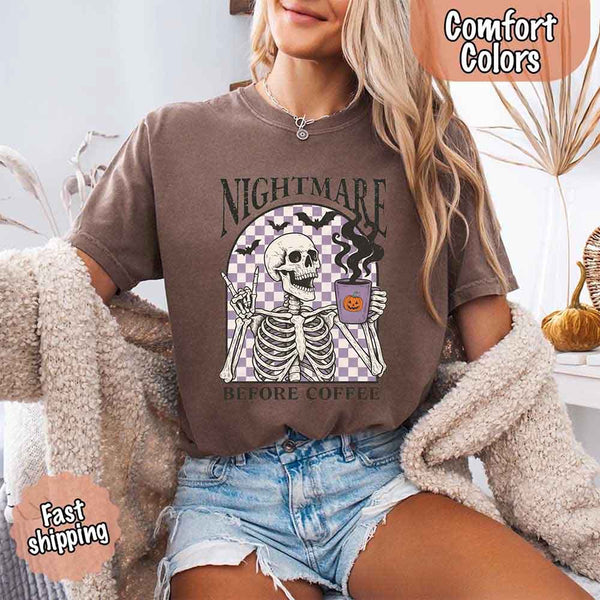 Nightmare Before Coffee skeleton graphic tee featuring skeleton holding a pumpkin coffee mug with steam, bats, and checkered background – funny Halloween coffee shirt.