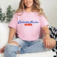 Woman wearing a pink t-shirt with 'Celebrating Freedom' text, sitting on a couch.