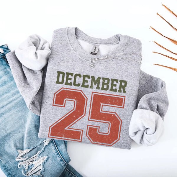 May include a retro-style Christmas sweatshirt featuring bold varsity lettering that reads “December 25” in green and red. The design has a vintage, slightly distressed look, giving it a nostalgic holiday feel perfect for festive winter wear.