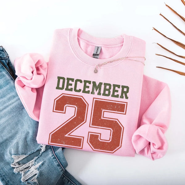 May include a retro-style Christmas sweatshirt featuring bold varsity lettering that reads “December 25” in green and red. The design has a vintage, slightly distressed look, giving it a nostalgic holiday feel perfect for festive winter wear.