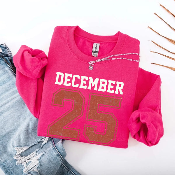 May include a retro-style Christmas sweatshirt featuring bold varsity lettering that reads “December 25” in green and red. The design has a vintage, slightly distressed look, giving it a nostalgic holiday feel perfect for festive winter wear.