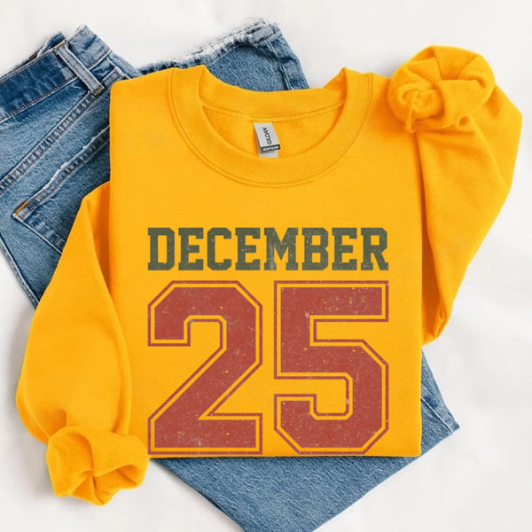 May include a retro-style Christmas sweatshirt featuring bold varsity lettering that reads “December 25” in green and red. The design has a vintage, slightly distressed look, giving it a nostalgic holiday feel perfect for festive winter wear.