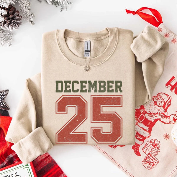 May include a retro-style Christmas sweatshirt featuring bold varsity lettering that reads “December 25” in green and red. The design has a vintage, slightly distressed look, giving it a nostalgic holiday feel perfect for festive winter wear.