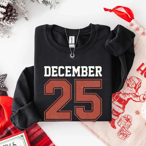 May include a retro-style Christmas sweatshirt featuring bold varsity lettering that reads “December 25” in green and red. The design has a vintage, slightly distressed look, giving it a nostalgic holiday feel perfect for festive winter wear.