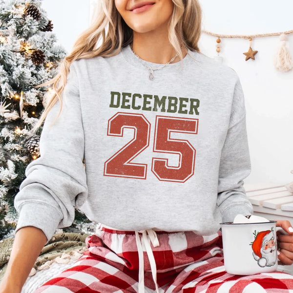 May include a retro-style Christmas sweatshirt featuring bold varsity lettering that reads “December 25” in green and red. The design has a vintage, slightly distressed look, giving it a nostalgic holiday feel perfect for festive winter wear.