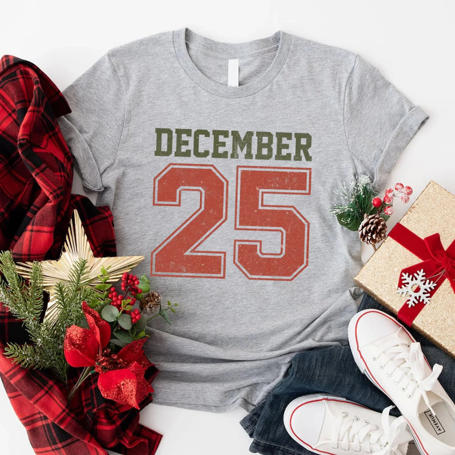 May include a retro-style Christmas sweatshirt featuring bold varsity lettering that reads “December 25” in green and red. The design has a vintage, slightly distressed look, giving it a nostalgic holiday feel perfect for festive winter wear.