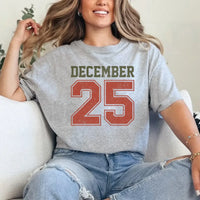 May include a retro-style Christmas sweatshirt featuring bold varsity lettering that reads “December 25” in green and red. The design has a vintage, slightly distressed look, giving it a nostalgic holiday feel perfect for festive winter wear.