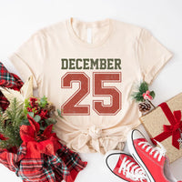 May include a retro-style Christmas sweatshirt featuring bold varsity lettering that reads “December 25” in green and red. The design has a vintage, slightly distressed look, giving it a nostalgic holiday feel perfect for festive winter wear.