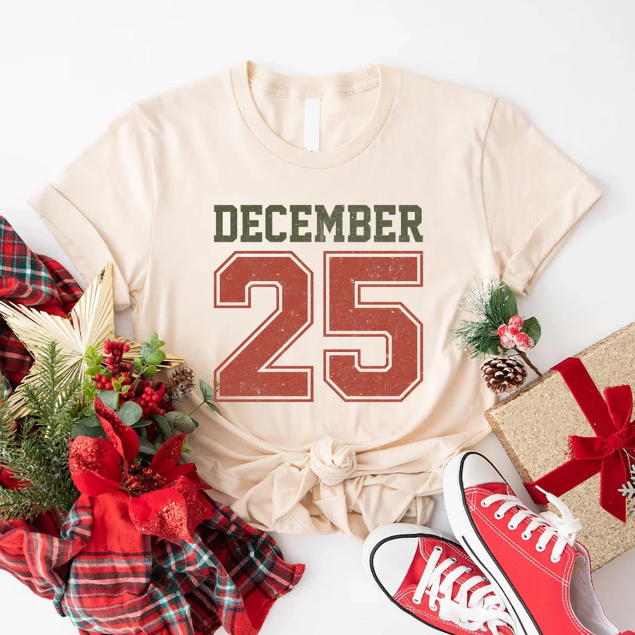 May include a retro-style Christmas sweatshirt featuring bold varsity lettering that reads “December 25” in green and red. The design has a vintage, slightly distressed look, giving it a nostalgic holiday feel perfect for festive winter wear.