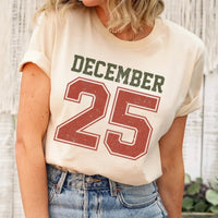 May include a retro-style Christmas sweatshirt featuring bold varsity lettering that reads “December 25” in green and red. The design has a vintage, slightly distressed look, giving it a nostalgic holiday feel perfect for festive winter wear.