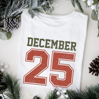May include a retro-style Christmas sweatshirt featuring bold varsity lettering that reads “December 25” in green and red. The design has a vintage, slightly distressed look, giving it a nostalgic holiday feel perfect for festive winter wear.