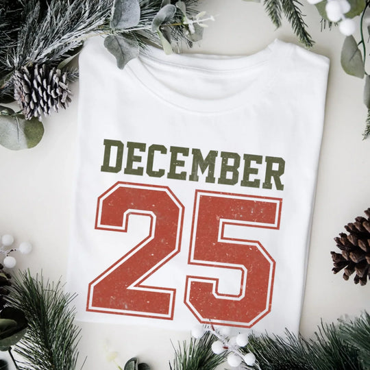 May include a retro-style Christmas sweatshirt featuring bold varsity lettering that reads “December 25” in green and red. The design has a vintage, slightly distressed look, giving it a nostalgic holiday feel perfect for festive winter wear.