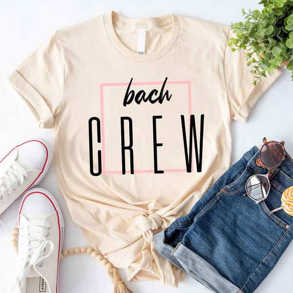 Beige t-shirt with 'bach CREW' text, paired with jeans, sneakers, and sunglasses on a white background.