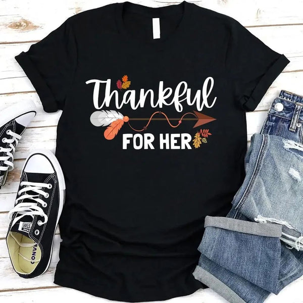 May include two matching Thanksgiving-themed T-shirts laid flat, one black reading “Thankful For Her” and one orange reading “Thankful For Him.” Both designs feature autumn leaves, feathers, and an arrow motif, surrounded by small pumpkins and fall decor.