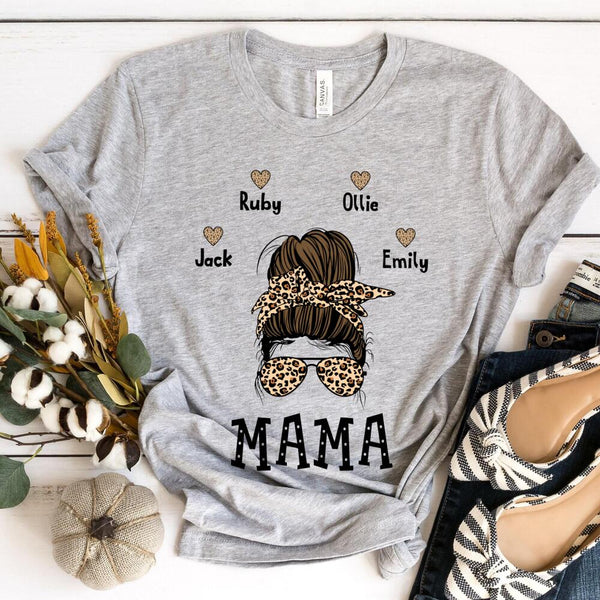Gray t-shirt with 'MAMA' and child names design on a white surface with decorative items.