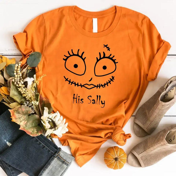 Orange t-shirt with a face design and text 'His Sally' on a white surface with accessories.