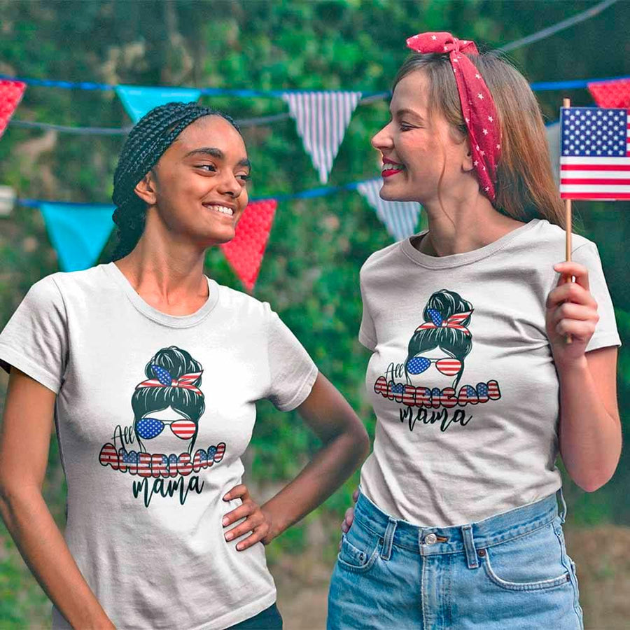 Two women wearing 'All American Mama' graphic tees at outdoor patriotic celebration with flags.