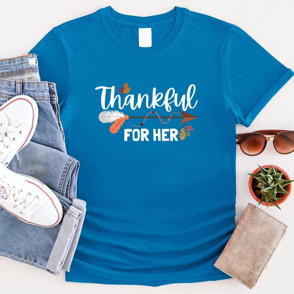 May include two matching Thanksgiving-themed T-shirts laid flat, one black reading “Thankful For Her” and one orange reading “Thankful For Him.” Both designs feature autumn leaves, feathers, and an arrow motif, surrounded by small pumpkins and fall decor.