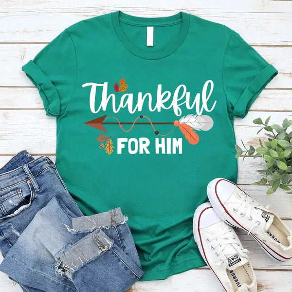 May include two matching Thanksgiving-themed T-shirts laid flat, one black reading “Thankful For Her” and one orange reading “Thankful For Him.” Both designs feature autumn leaves, feathers, and an arrow motif, surrounded by small pumpkins and fall decor.