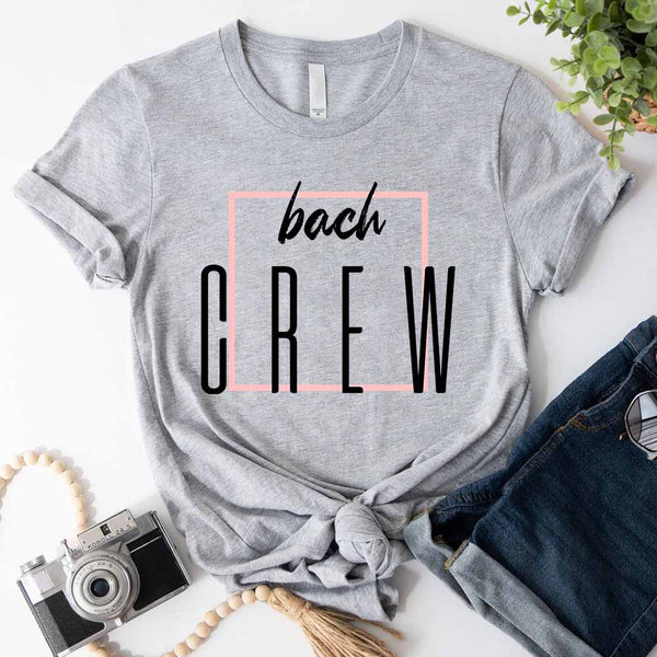 Gray t-shirt with 'bach CREW' text on a white surface with accessories.