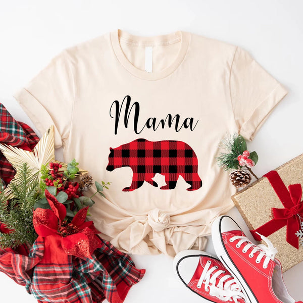 May include matching family t-shirts featuring a Christmas bear design, laid flat with festive decorations and greenery.