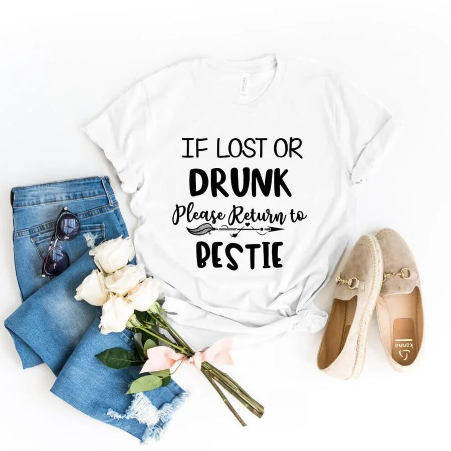 White t-shirt with 'If lost or drunk, please return to bestie' text, paired with jeans, sunglasses, flowers, and shoes on a white background.