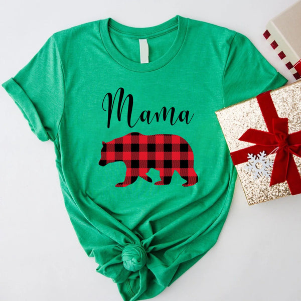 May include matching family t-shirts featuring a Christmas bear design, laid flat with festive decorations and greenery.