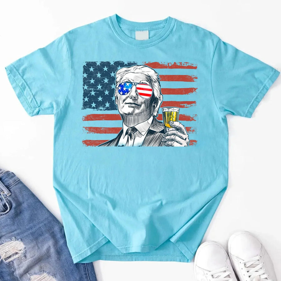 Light blue t-shirt with graphic design of a person holding a shot glass with an American flag filter, displayed on a white background.