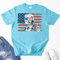 Light blue t-shirt with graphic design of a person holding a shot glass with an American flag filter, displayed on a white background.