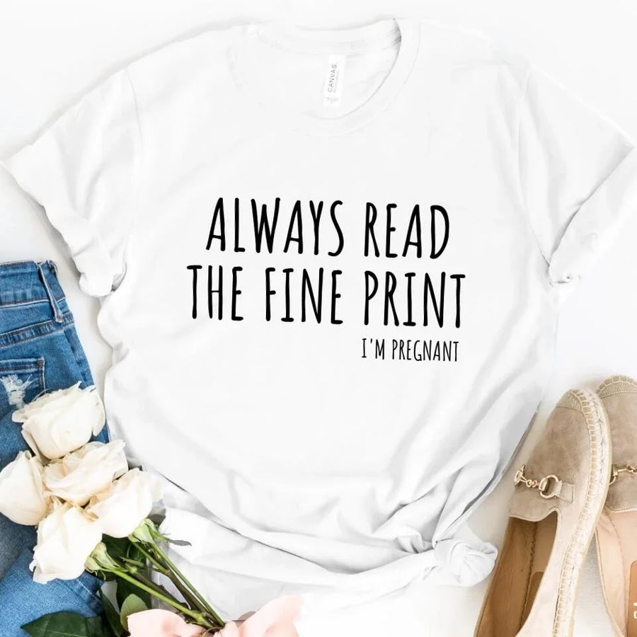 White custom tee with 'Always Read The Fine Print I'm Pregnant' text, flat lay with jeans, roses, and shoes