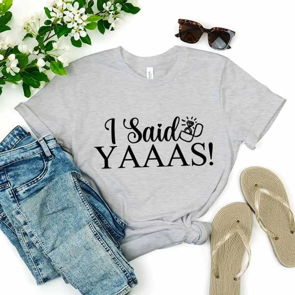 Gray t-shirt with 'I Said YAAAS!' text, paired with denim shorts and flip-flops on a white background.