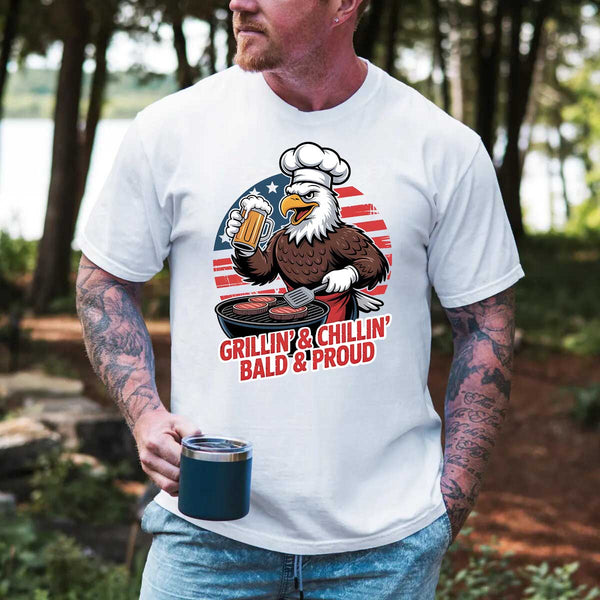 Person wearing a white t-shirt with an eagle graphic and text, holding a mug outdoors.