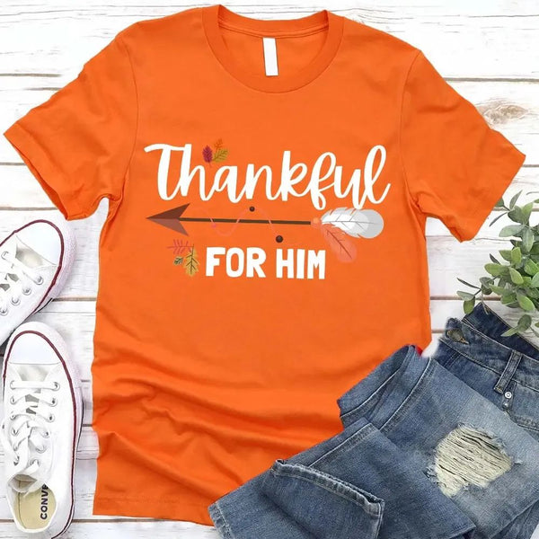 May include two matching Thanksgiving-themed T-shirts laid flat, one black reading “Thankful For Her” and one orange reading “Thankful For Him.” Both designs feature autumn leaves, feathers, and an arrow motif, surrounded by small pumpkins and fall decor.