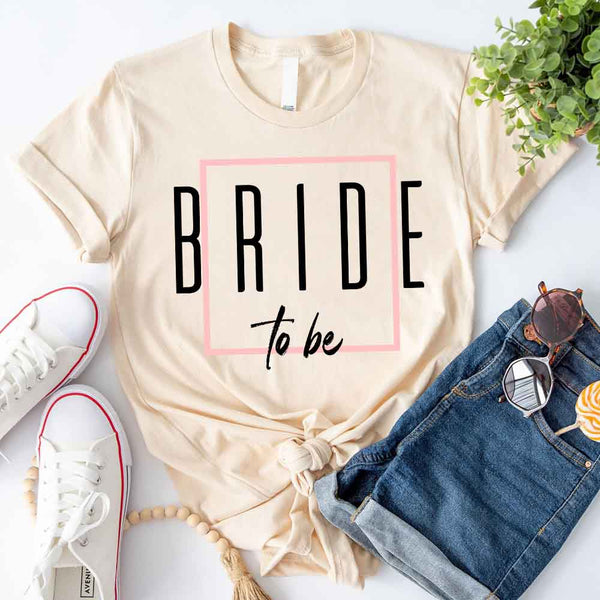 Beige t-shirt with 'BRIDE to be' text, white sneakers, denim shorts, and sunglasses on a light background