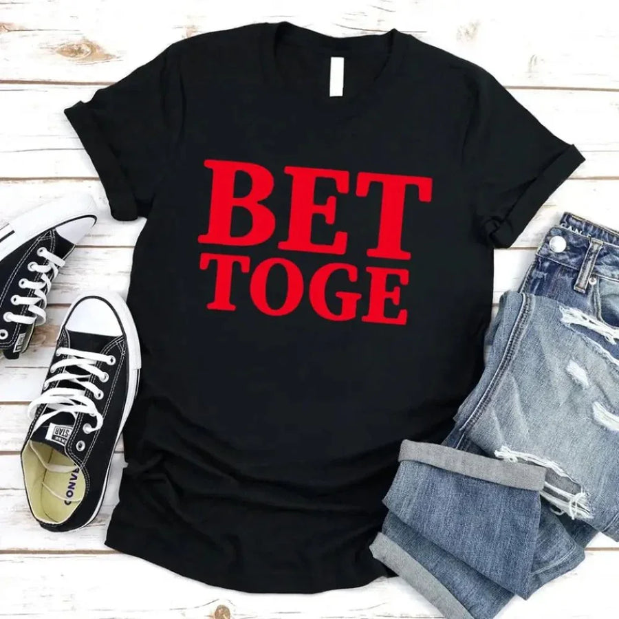 Black t-shirt with red text 'BET TOGE', black sneakers, and denim shorts on a wooden surface.