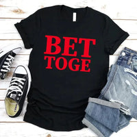 Black t-shirt with red text 'BET TOGE', black sneakers, and denim shorts on a wooden surface.