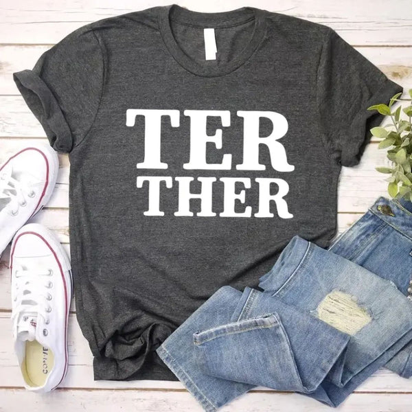 Gray t-shirt with 'TER THER' text, paired with jeans and sneakers on a wooden surface.