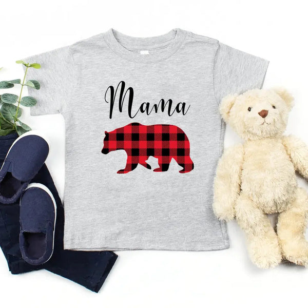 May include matching family t-shirts featuring a Christmas bear design, laid flat with festive decorations and greenery.