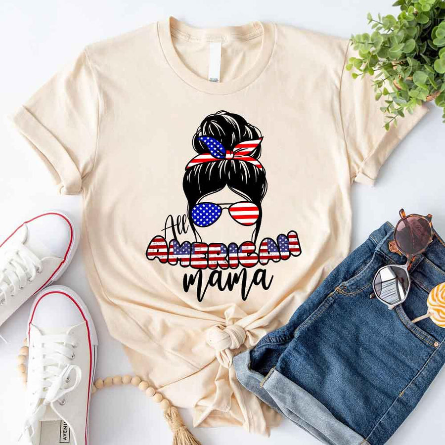 Beige patriotic graphic tee with 'All American Mama' and USA flag print, styled with denim shorts