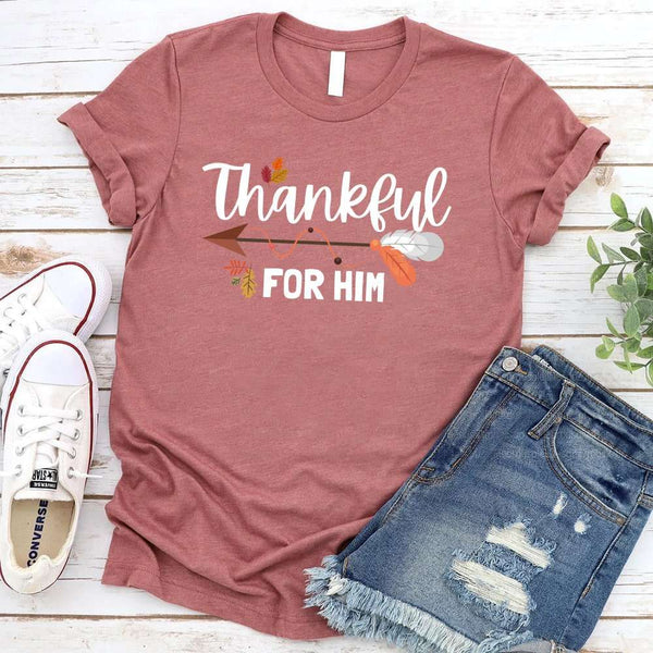 May include two matching Thanksgiving-themed T-shirts laid flat, one black reading “Thankful For Her” and one orange reading “Thankful For Him.” Both designs feature autumn leaves, feathers, and an arrow motif, surrounded by small pumpkins and fall decor.
