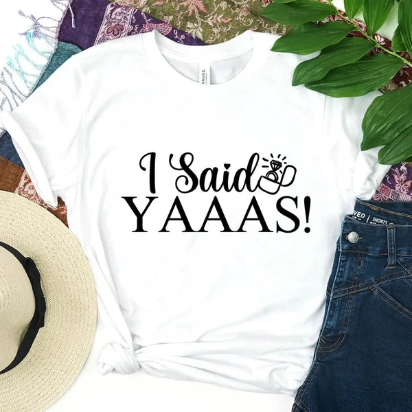 White t-shirt with 'I Said YAAAS!' text, surrounded by a hat, jeans, and decorative elements.
