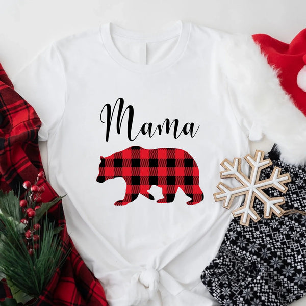 May include matching family t-shirts featuring a Christmas bear design, laid flat with festive decorations and greenery.