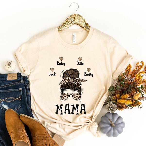 Beige t-shirt with 'MAMA' and names printed, displayed with jeans, boots, and decorative items.