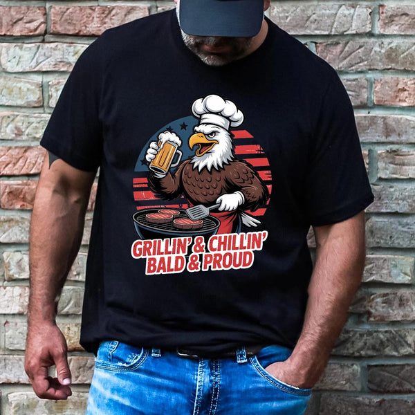 Person wearing a black t-shirt with an eagle graphic and text 'Grillin & Chillin' Bald & Proud' against a brick wall.