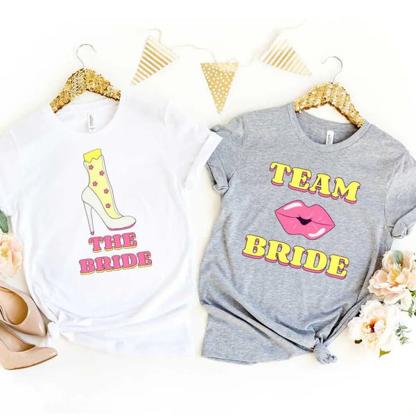 Two t-shirts with 'The Bride' and 'Team Bride' text on hangers against a white background.