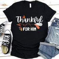 May include two matching Thanksgiving-themed T-shirts laid flat, one black reading “Thankful For Her” and one orange reading “Thankful For Him.” Both designs feature autumn leaves, feathers, and an arrow motif, surrounded by small pumpkins and fall decor.