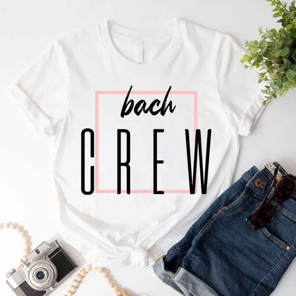 White t-shirt with 'bach CREW' text on a white surface with denim shorts and sunglasses.